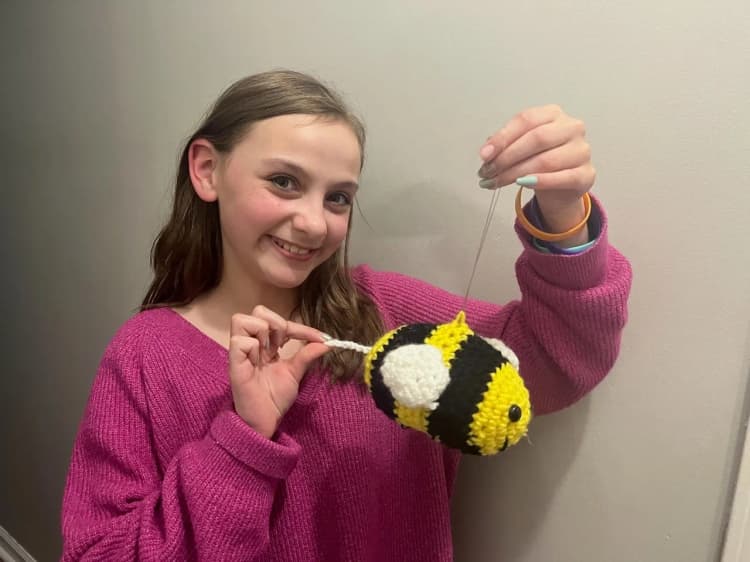 Seren, the young maker behind Blue Sky Pet Products, holding a handmade crocheted bee